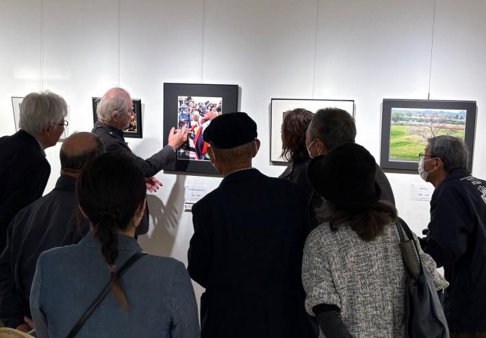 令和6年度取手市民美術展2部合評会の様子。壁に飾られた写真の前で、多くの人が集まり鑑賞している。