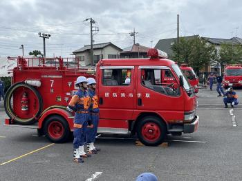 消防服を着て消防車の横に並ぶ男性2名