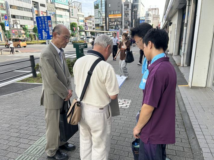 アンケートの説明をする学生とアンケートを書く男性