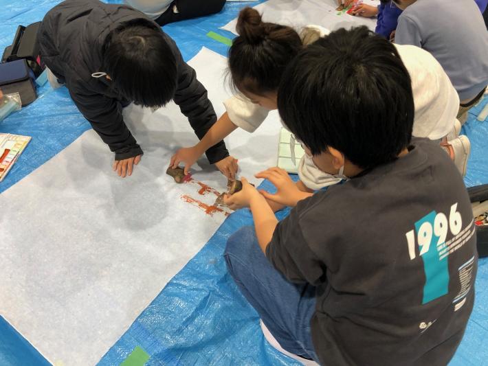 和紙の上に桜の木を並べる子どもたちと桜の木のスタンプを和紙におす子どもたち