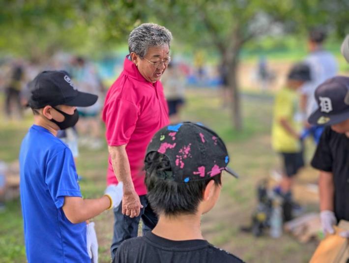 ピンク色のポロシャツを着た男性が、火の着火台をくみ上げる様子をみている