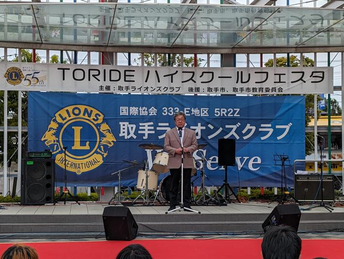 「TORIDE ハイスクールフェスタ」と書かれた看板の下であいさつをする市長