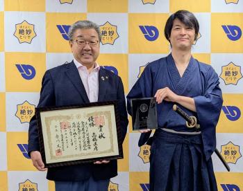 道着を着て刀を携帯する男性とスーツを着た男性