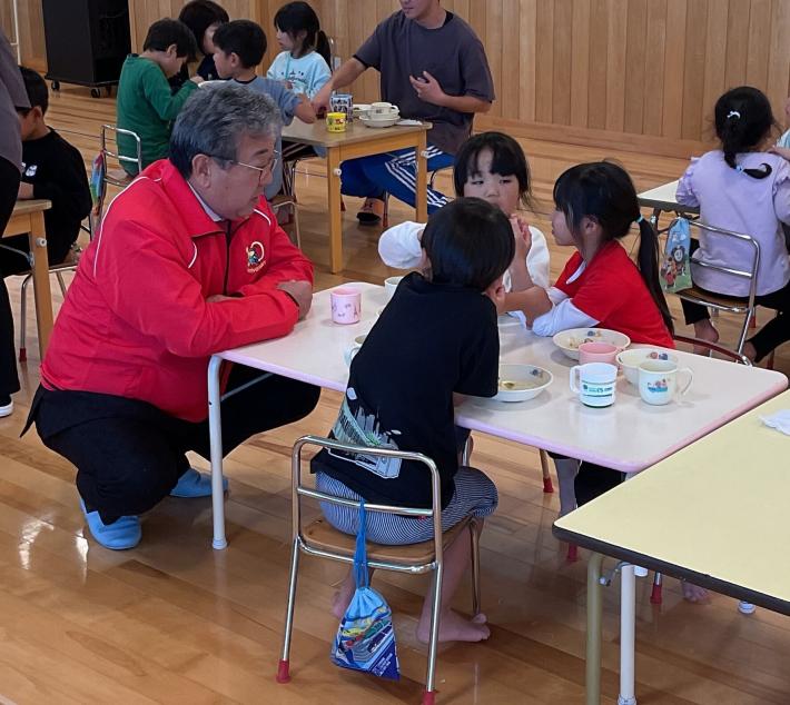 給食を食べる子どもにかがんで話しかける男性