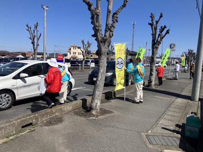 赤と黄色のジャンパーを着た人が車両にのった人に声掛けをしている