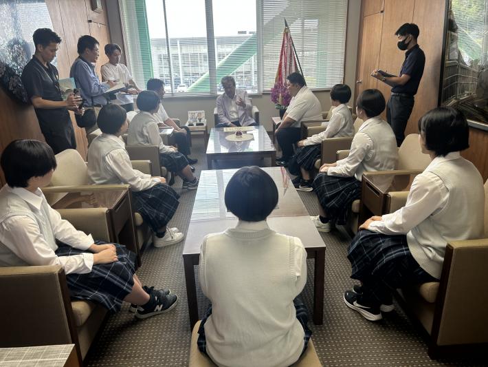 テーブルを囲んで座る男性たちと制服を着た女子学生