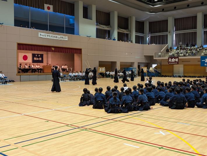 剣道着を着た子どもたちが座って剣道の演武をみている