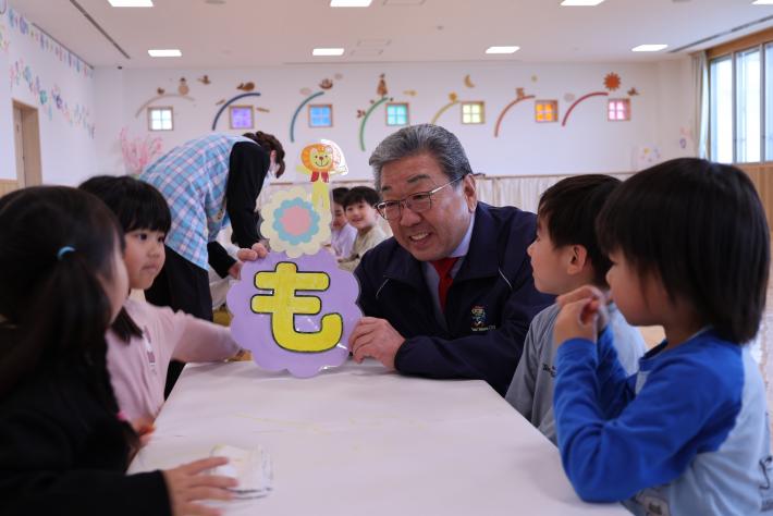 「も」の文字をもって子どもたちに話しかける市長