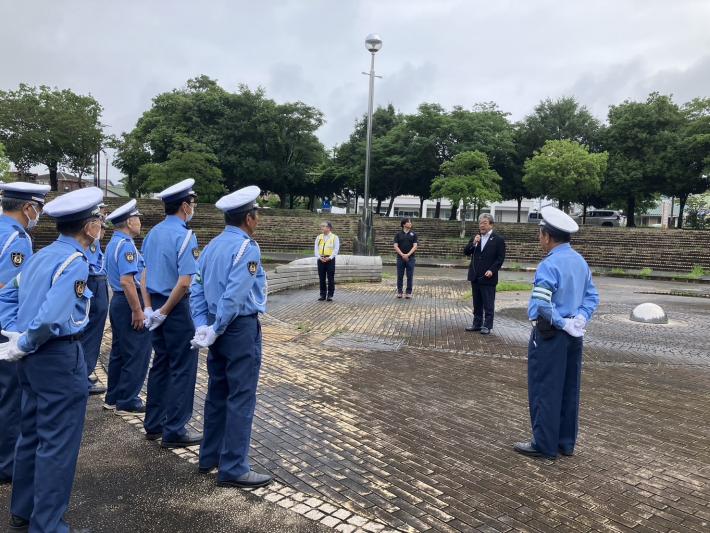 外の大きな広場で制服を着た人たちに向けてあいさつをする男性