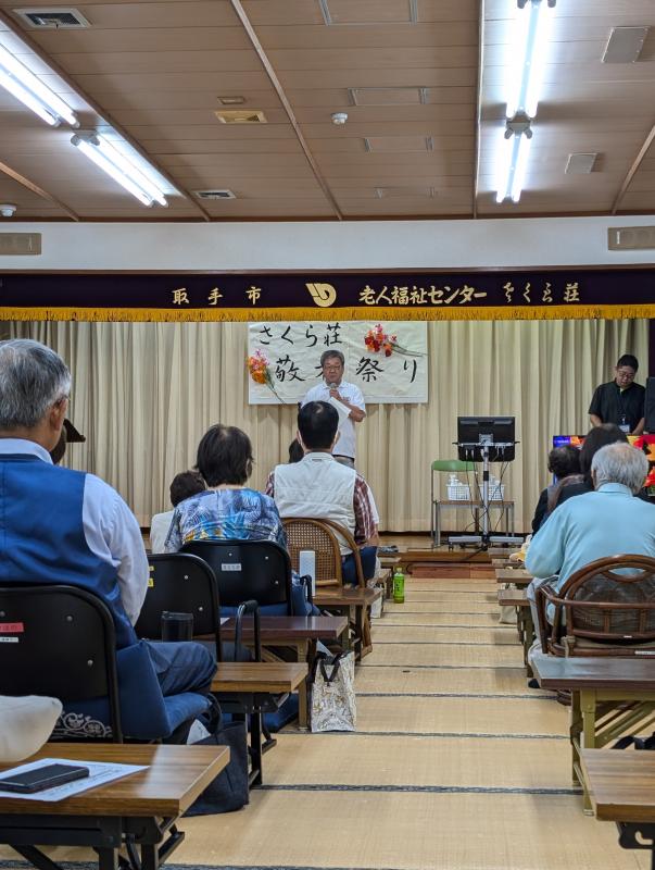 さくら荘敬老まつりと書かれた看板の下からあいさつをする男性