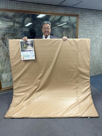 茶色いシートを持って立つ男性