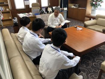 四角いテーブルの前で座る学生3名と男性