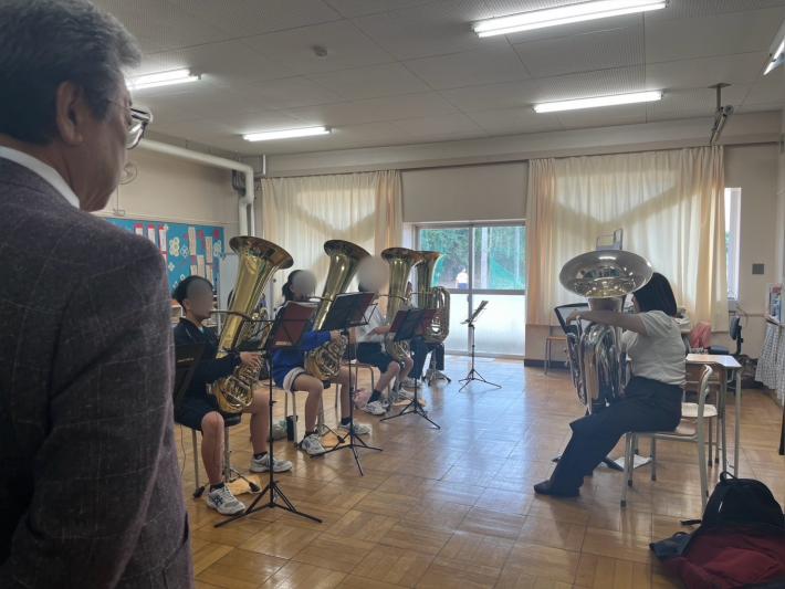 トロンボーンを座って吹く学生たちと大人