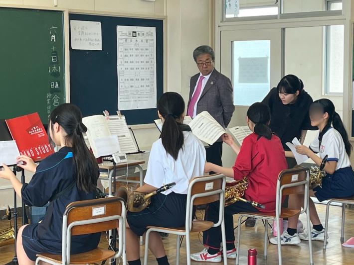 座って金管楽器を吹く学生に助言をする大人