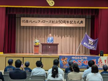 藤代バッファローズ創立50周年記念式典と書かれた看板の下から挨拶をする男性