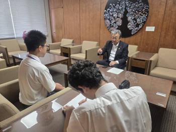 机を挟んで向かい合う学生2名と大人の男性
