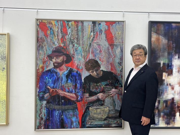 陶芸をする2人を描いた絵画の横に立つ男性