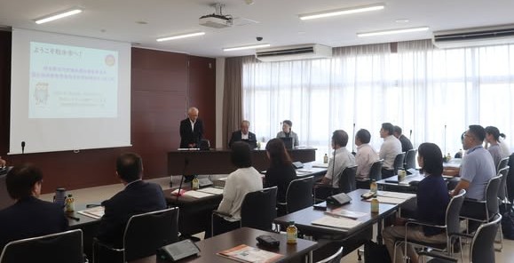 会議室で10数名の男性と女性が椅子に座って、話を聞いている