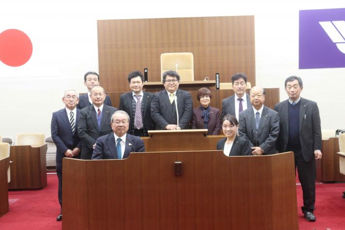 宮崎県小林市議9名と取手市議2名が取手市議会議場の壇上および書記席付近で記念撮影をしている様子