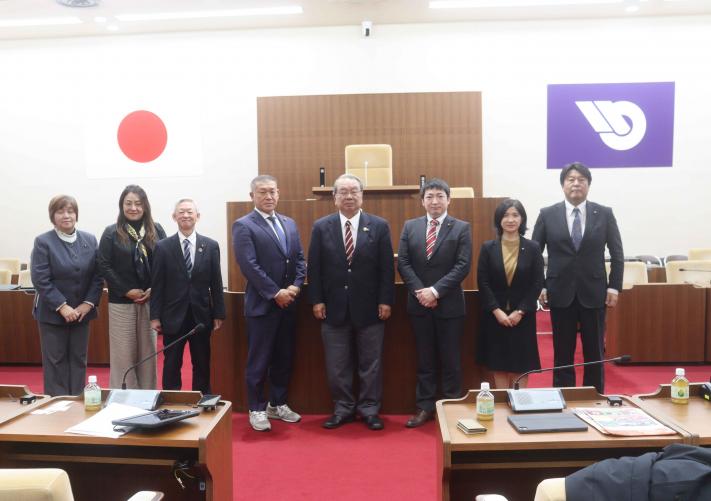 静岡県藤枝市議6名と取手市議2名が取手市議会議場の書記席前に横一列に並んで記念撮影をしている様子