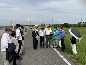 小貝川の過去の決壊箇所の土手上で視察する7人の議員と職員の写真