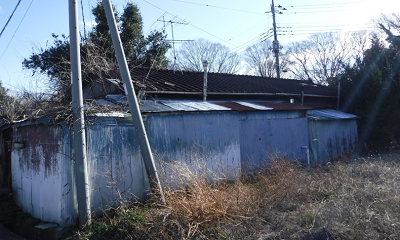 平屋の住居。本来の家の周りに、増築されたと思われるゆがんだ白色トタンの壁と屋根が映る