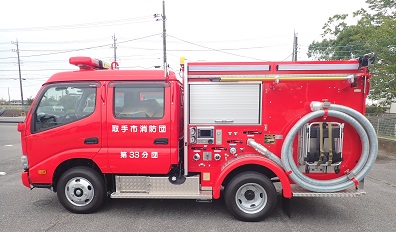 駐車場に停められた赤色の消防団自動車。左側面から写真を撮る。後ろ側に巻かれたホースが見える