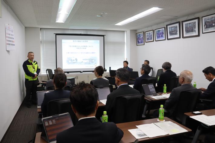 会議室で常総市役所の職員が取手市議会総務文教常任委員の前に立って研修を行っている