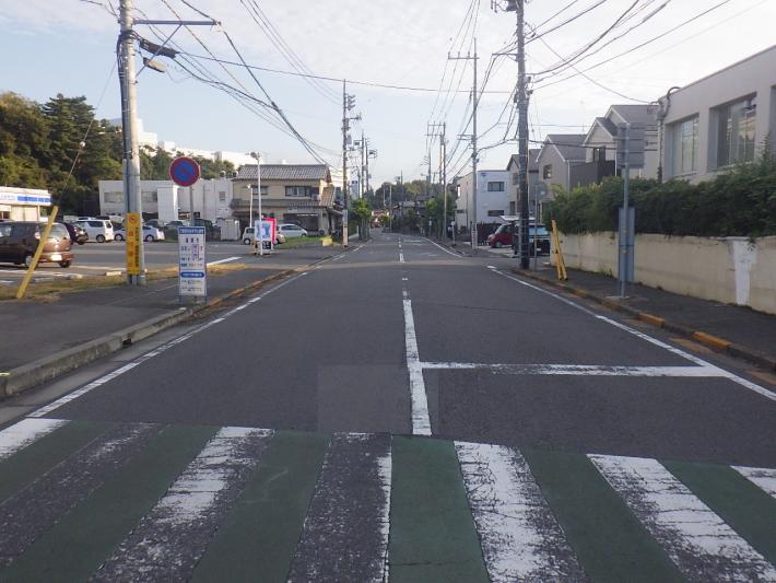 左にコンビニがあり、右に建物がある。横断歩道の白い部分は半分近く消えている。