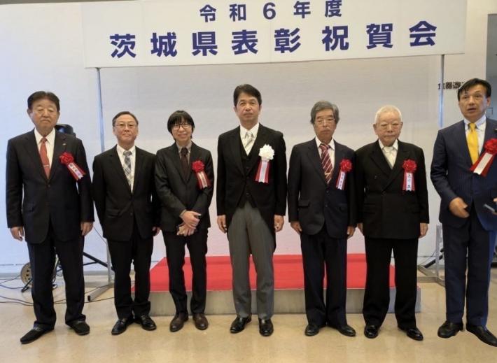 「令和6年度茨城県表彰祝賀会」の横看板の前で集合写真を撮る7名の男性