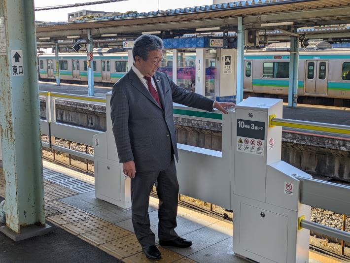 駅のホームにてホームドアに手をかけ眺める市長