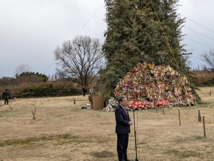 屋外芝生にて挨拶をする市長。背景には高く積み上げられた正月飾り