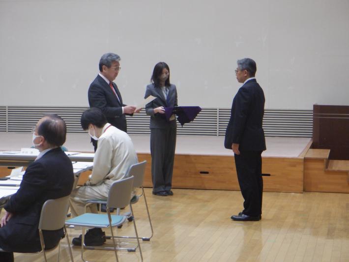 ホールにて委嘱状を交付する市長と介添えの職員。市長の前に委嘱されるスーツの男性