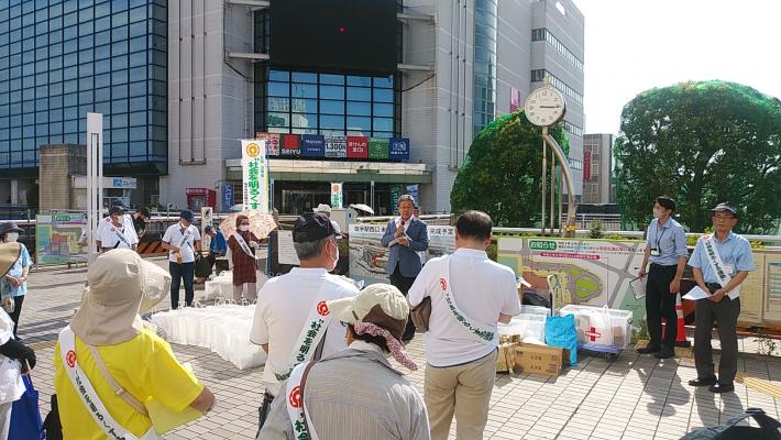 社会を明るくする運動の参加者に市長が話をしている。たすきをかけた人たちが市長の前側で立って話を聞いている。