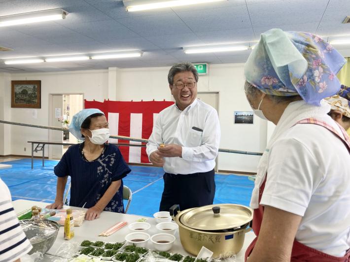 高須ふれあいフェスティバルの画像。ブルーシートが貼られ、後ろ壁に紅白幕のかかった部屋でエプロン姿の女性2人と談笑する男性。