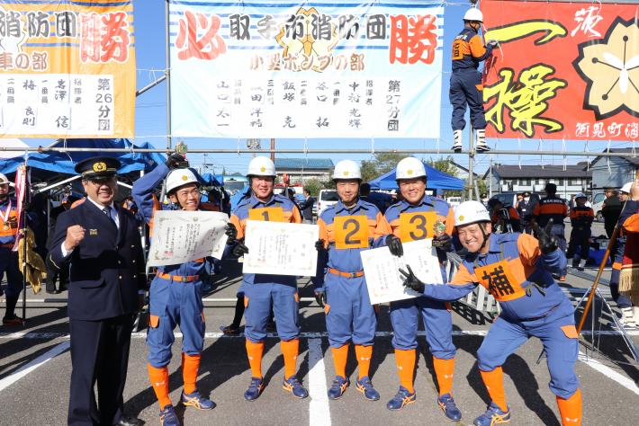 横断幕の前で消防服を着た5人の団員と市長が立っている