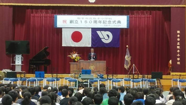 小学校の体育館にて、ステージ上演台で挨拶をする市長