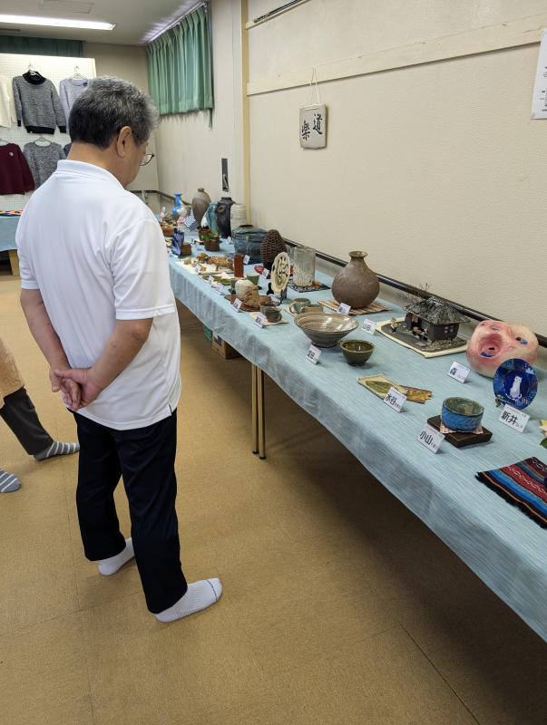 机に並べられたたくさんの陶芸作品を鑑賞する男性