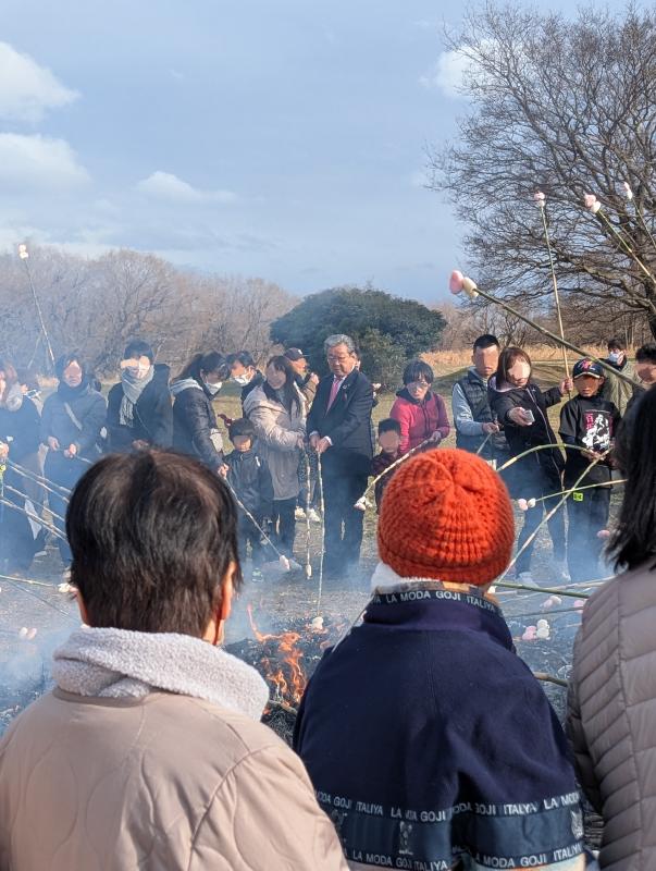 多くの人が焚火を囲んで長い棒を差し込んでいる