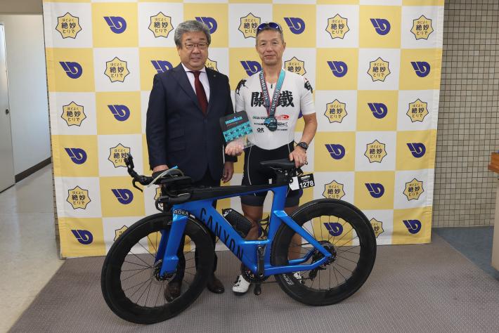 自転車の前に立つスーツを着た男性とユニフォームを着た男性