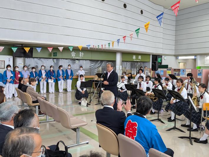 学生吹奏楽部を後ろにあいさつをする男性