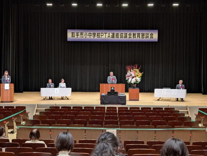 取手市小中学校PTA連絡協議会教育懇談会と書かれた看板の下からあいさつをする男性