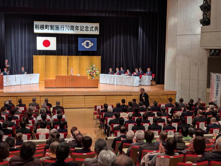 着座の多くの参加者に向けて、立っておじぎをする男性