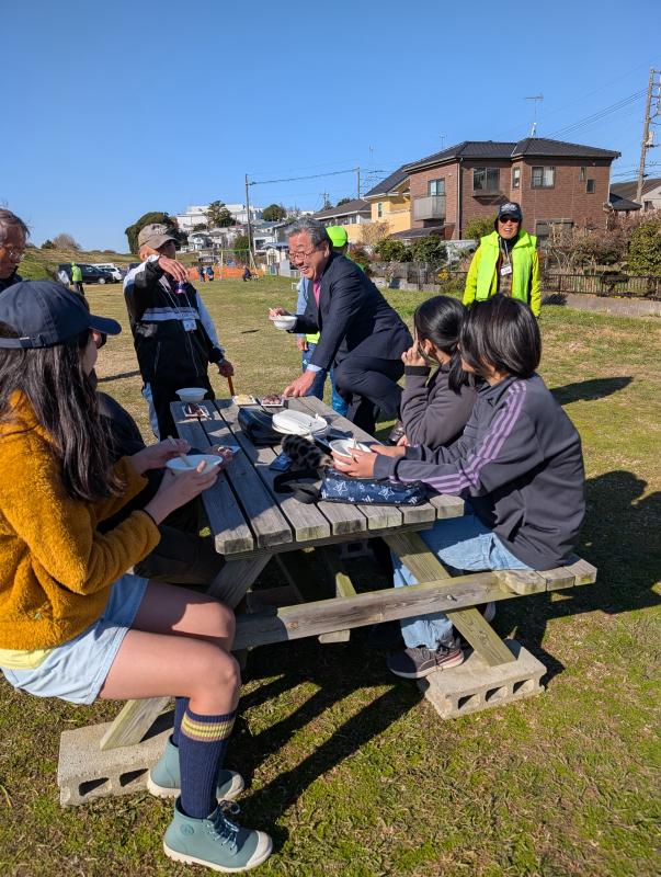 木製の椅子に座る子どもたちと子どもたちに話しかける男性