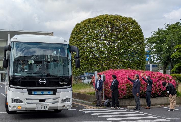 出発するバスに向けて手を振る市長