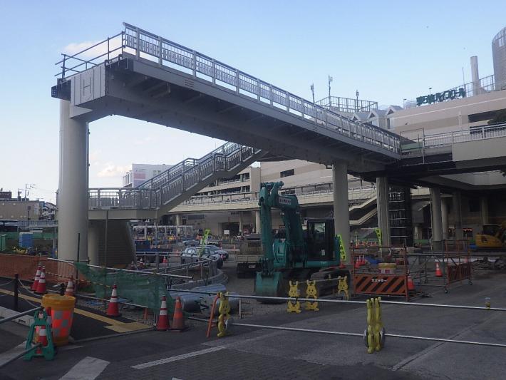 工事中の歩道橋と緑色のショベルカーの写真