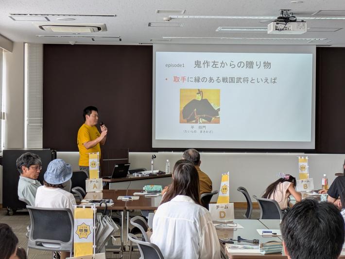 黄色い服の男性がスライドを使って、会員の皆さんに説明している様子