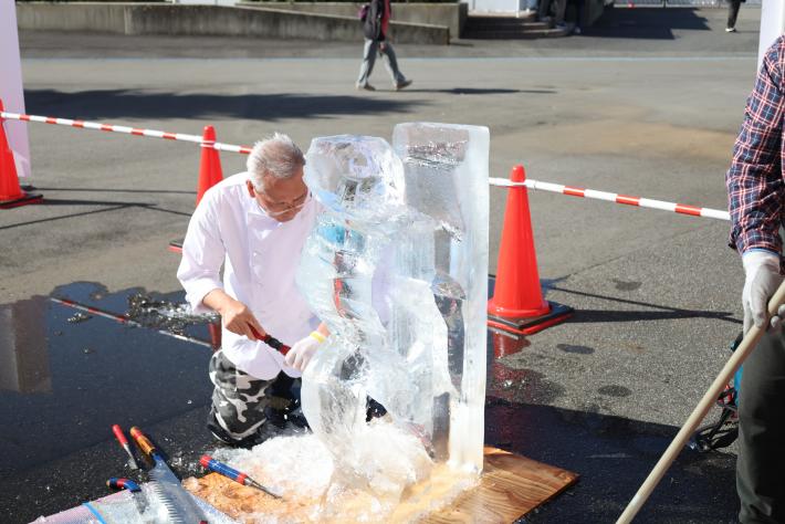 膝を地面について氷をのこぎりで削っている男性選手