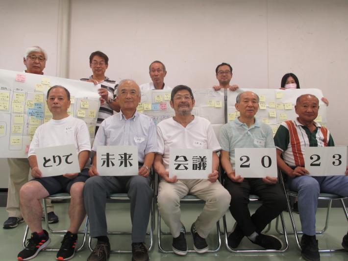 とりで未来会議（取手会場）の集合写真。手にそれぞれ文字などがかかれた紙を持ち、2列に並んで皆で記念撮影する様子