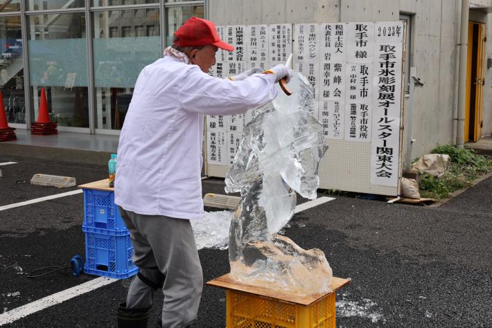 赤い帽子を着用しのこぎりを持った男性が氷を削っている